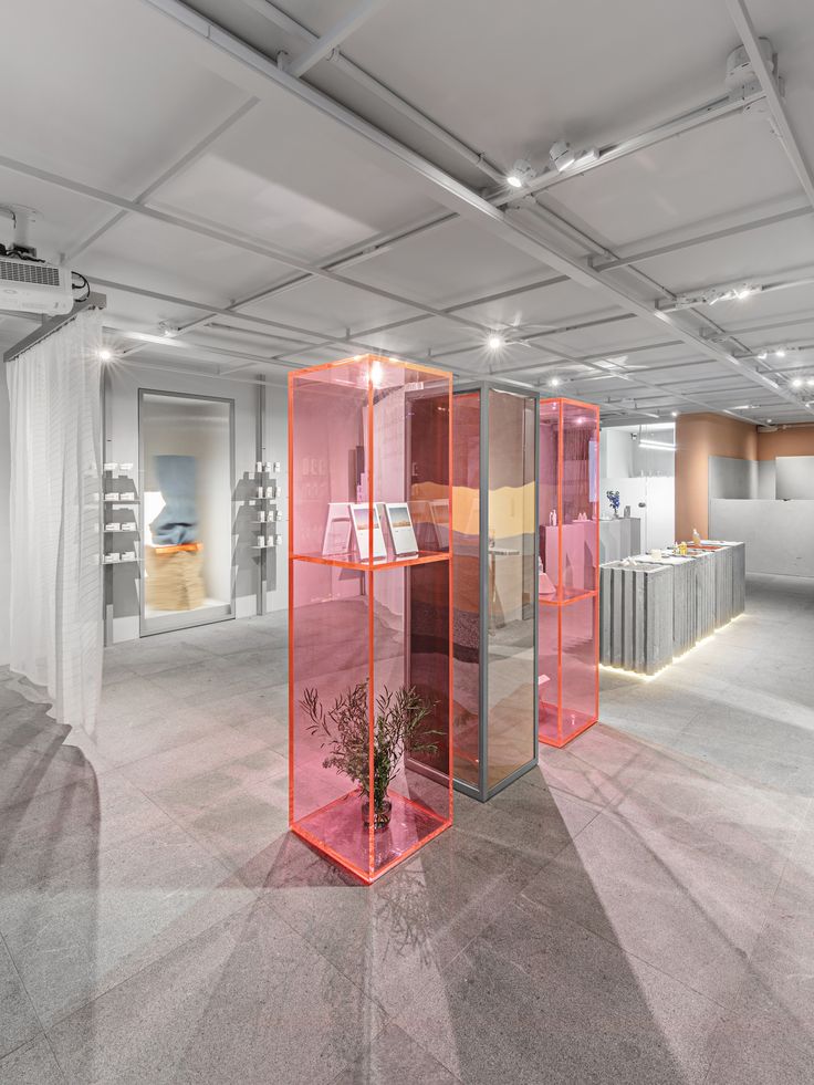 an empty room with several different colored glass cases on the floor and plants in vases