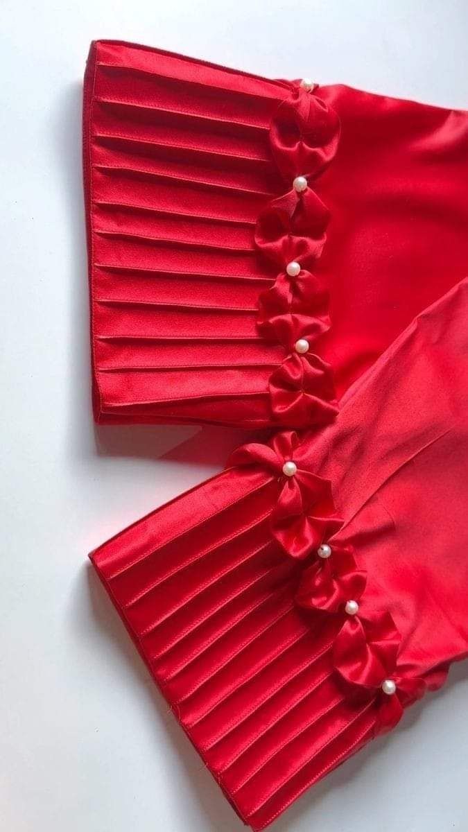 two red blouses with pearls on them sitting on a white surface, one is folded up and the other has pleated fabric