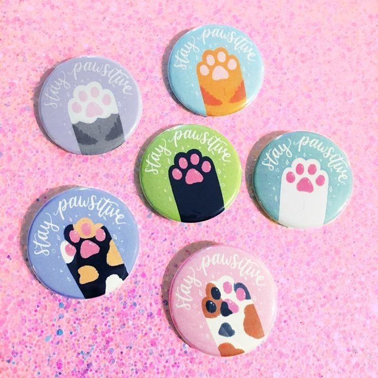 four buttons with paw prints on them sitting on a pink surface and the words my pawstuff are written in different languages