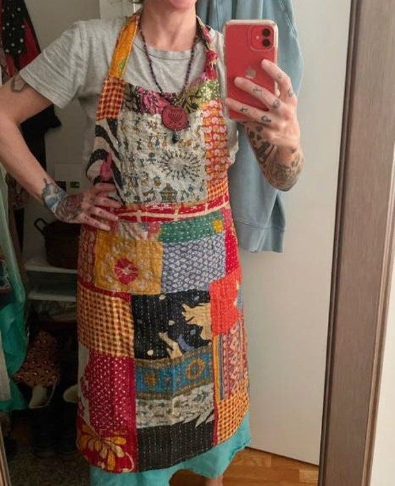 a woman taking a selfie in front of a mirror wearing an apron and holding a cell phone