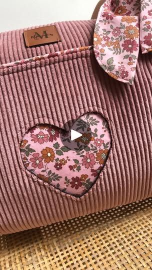 a pink purse with a heart shaped patch on the front and bow at the top