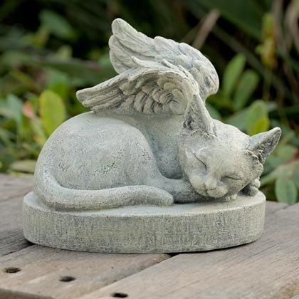 a statue of a cat with angel wings on it's head sitting on a rock