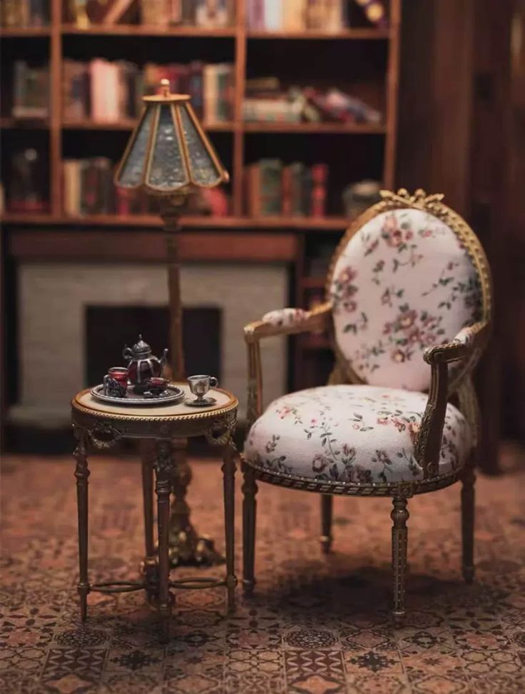 a miniature chair and table in front of a bookshelf with a lamp on it