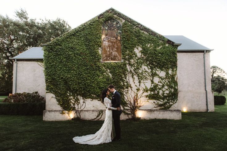 a bride and groom standing in front of a building with ivy growing on it's side