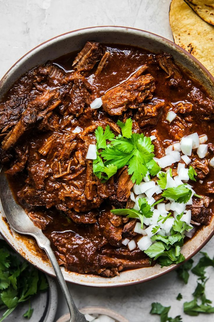 a bowl filled with beef and cilantro next to tortilla chips