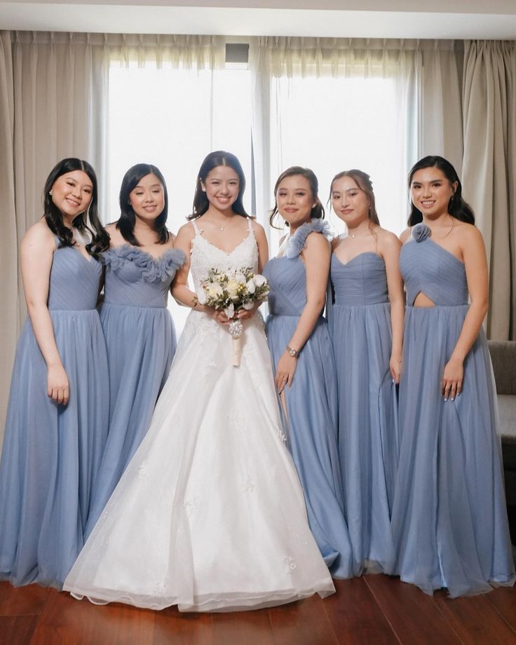 a group of women standing next to each other in front of a window wearing blue dresses