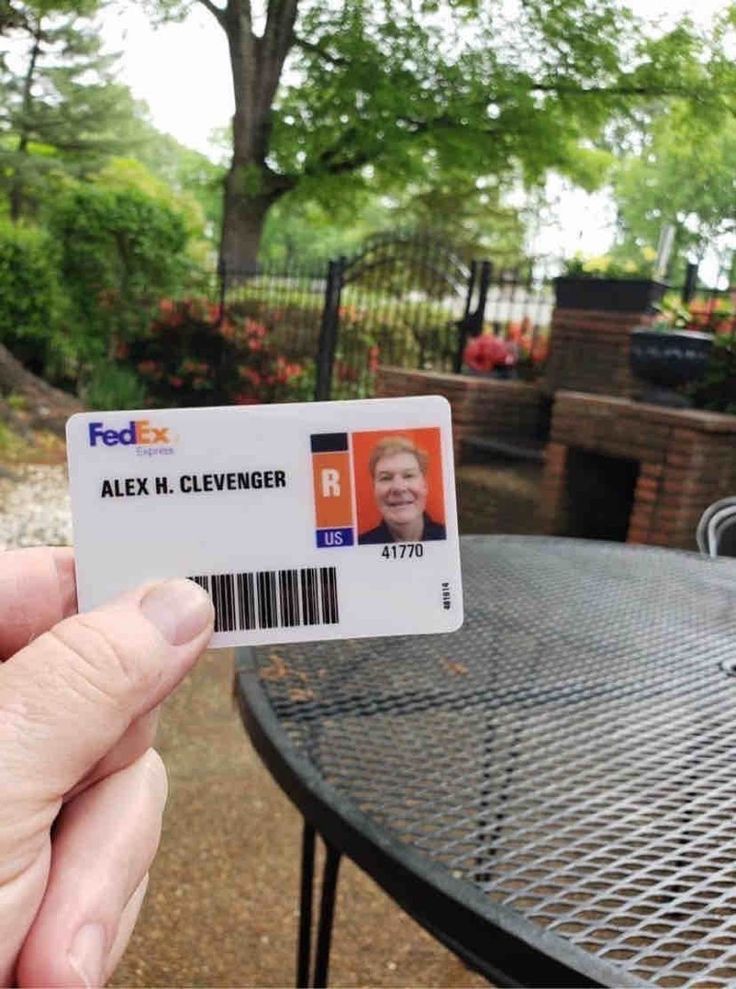 a person holding up a business card in front of a table with chairs and trees