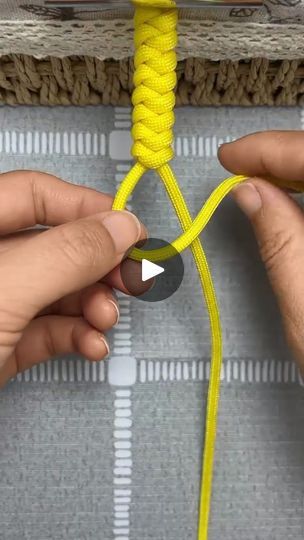 two hands are tying a yellow rope to a piece of fabric on a table top