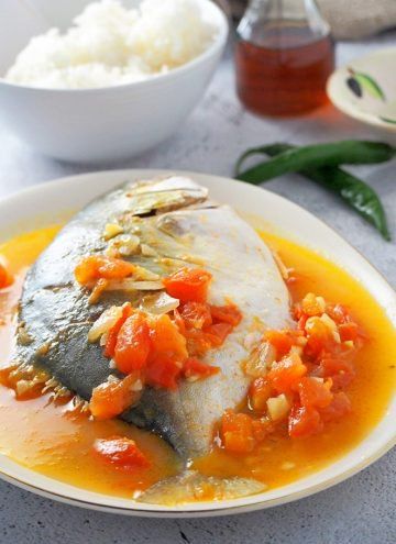 a white plate topped with fish covered in sauce and vegetables next to rice on a table