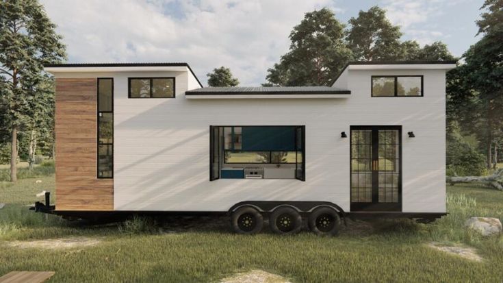 a tiny house on wheels in the middle of a grassy area with trees and rocks