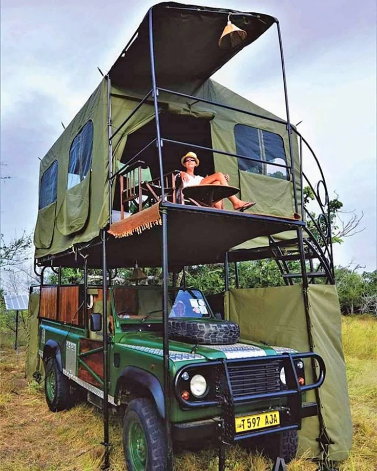 a green truck with a tent on top and people sitting in the bed above it