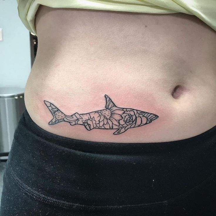 a woman's stomach with a tattoo of a shark and flowers on the side