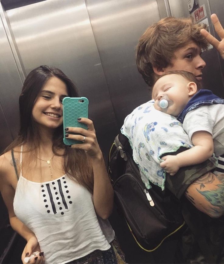 a woman holding a baby and taking a selfie in an elevator with her cell phone