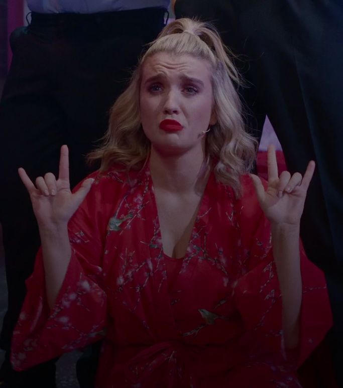 a woman in a red dress is making the peace sign with her hands while sitting down