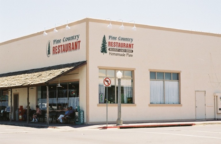 a restaurant with people sitting at the tables outside and an empty parking lot in front of it