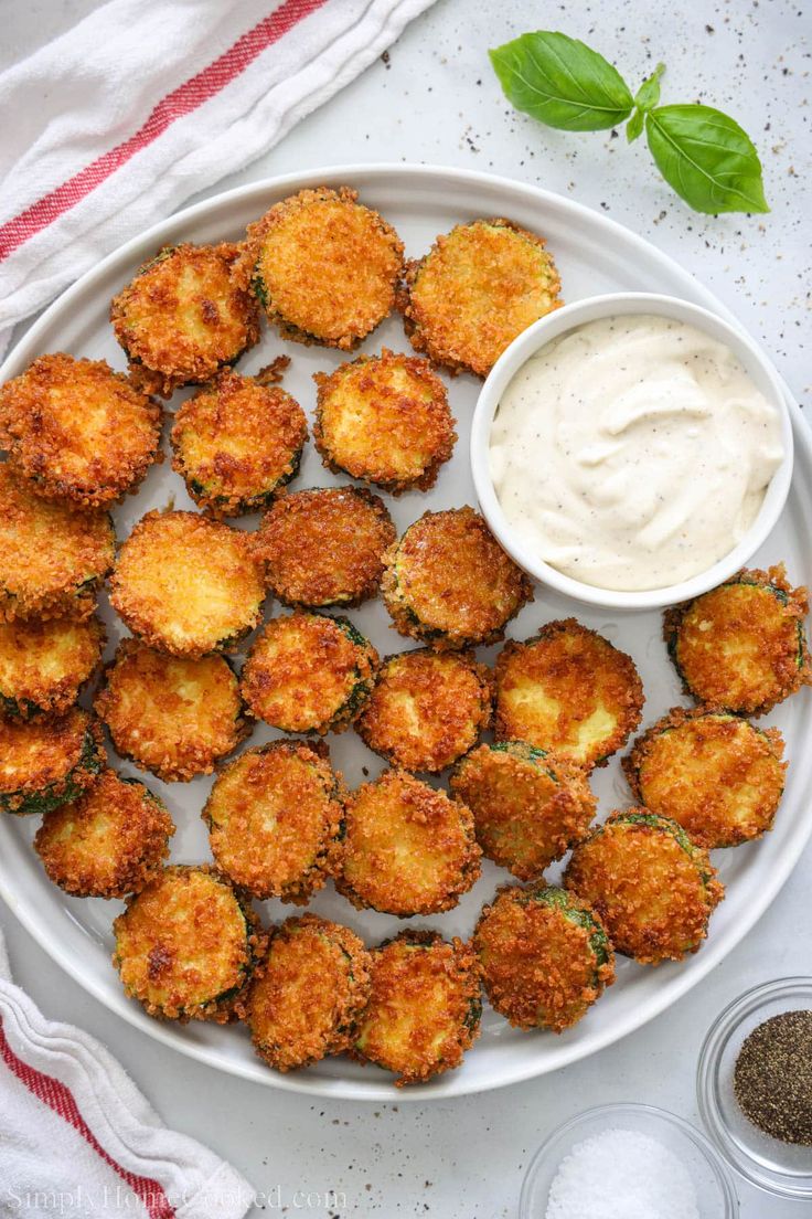 a white plate topped with fried food next to a bowl of ranch dressing