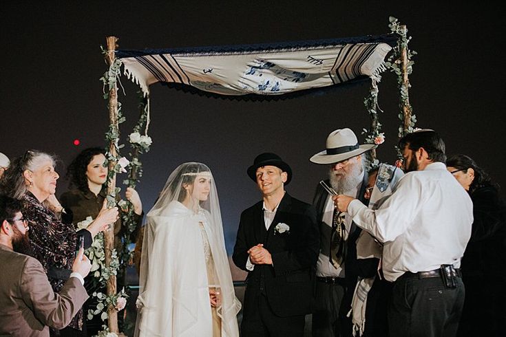 a bride and groom are standing under an umbrella at their wedding ceremony with other people around them