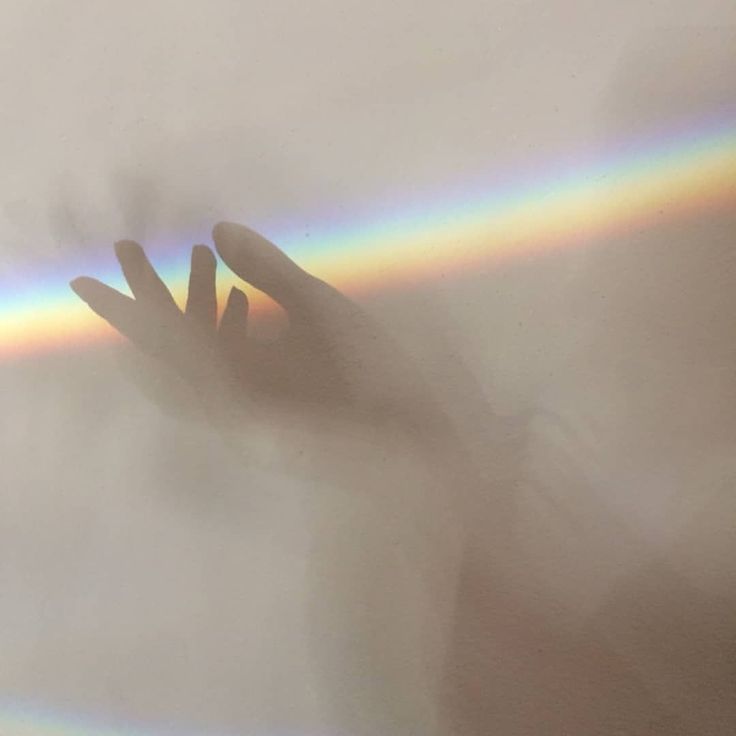 a person's hand reaching up into the sky with a rainbow in the background