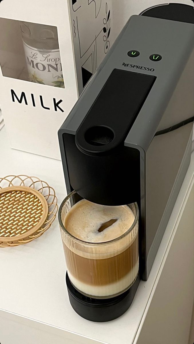 a coffee maker sitting on top of a counter next to a glass filled with liquid