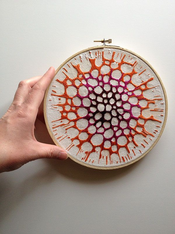 a hand holding up a small embroidery project on a white surface with orange and pink designs