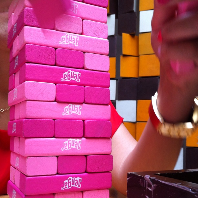 a stack of pink blocks sitting on top of a table next to a woman's hand