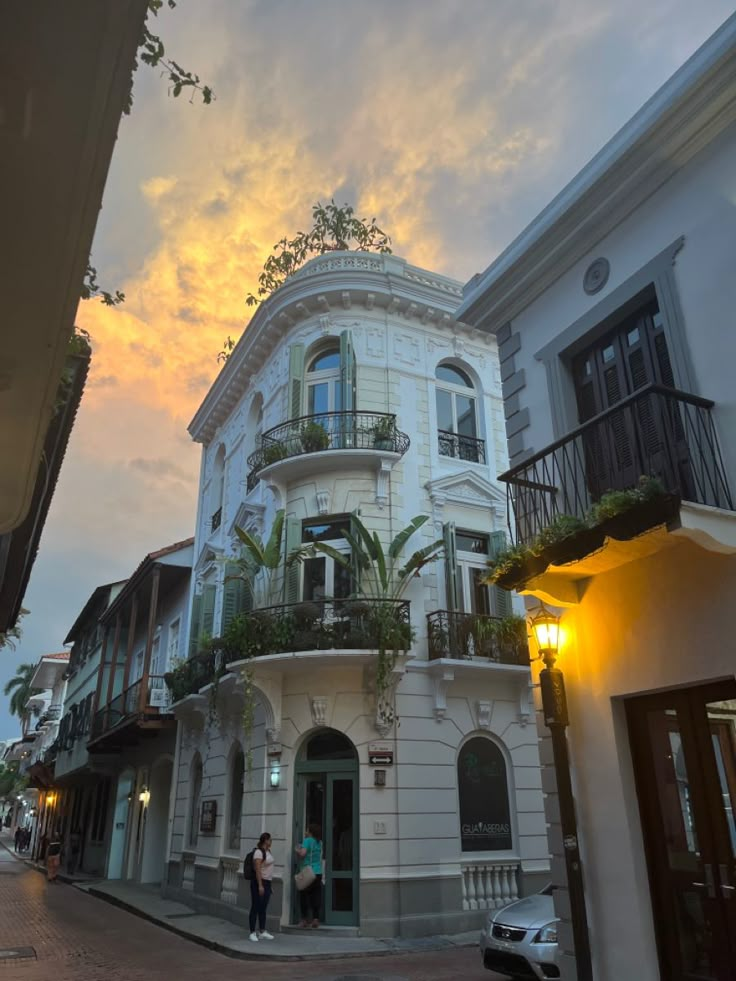 two people standing in front of a building with balconies and plants on it