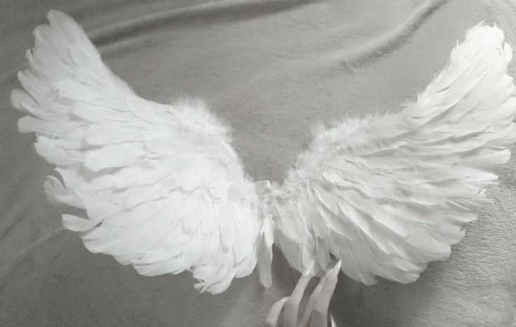 a white angel wing is being held by someone's hand on a gray blanket