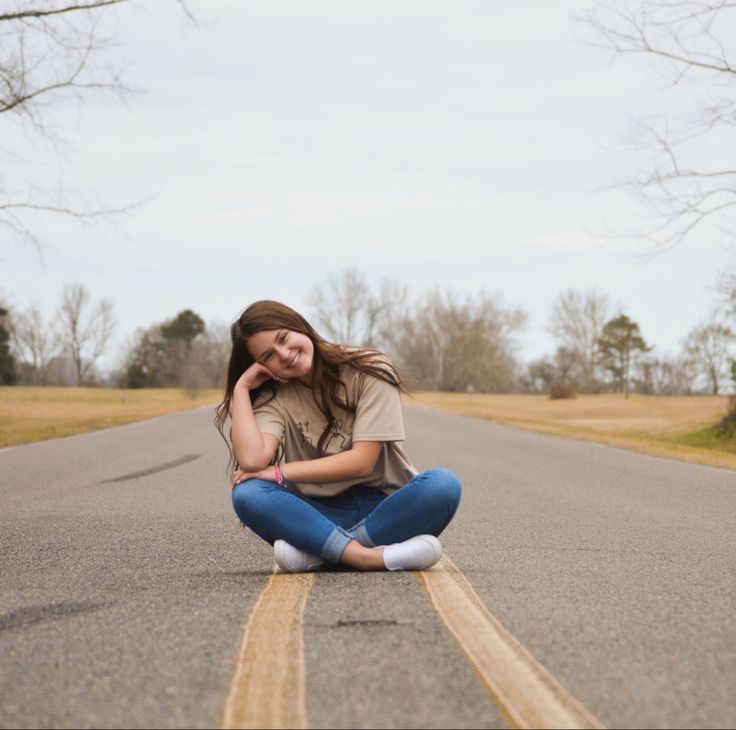 a young woman sitting on the side of an empty road with her hands behind her head