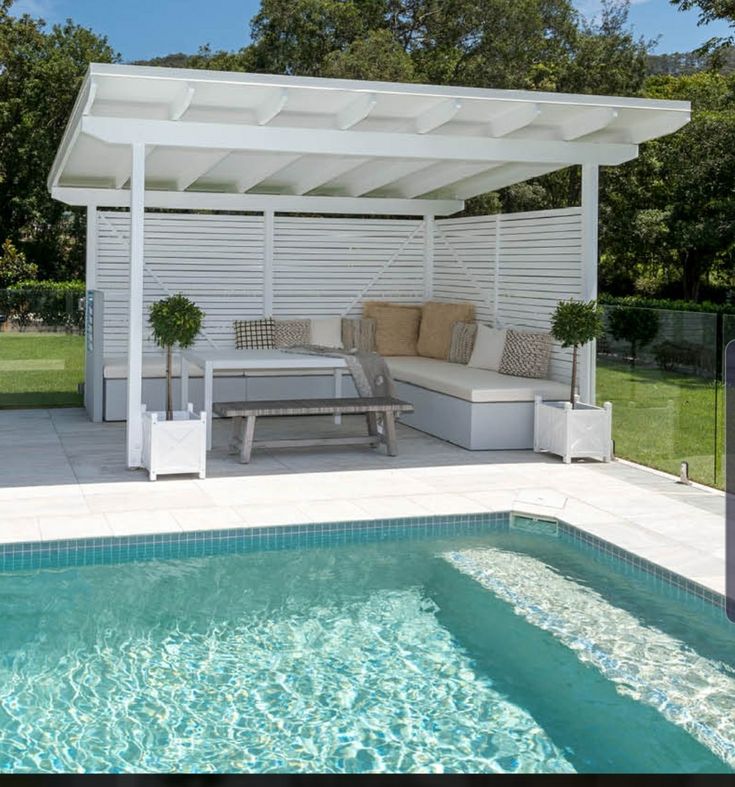 a white pergoline covered patio next to a swimming pool