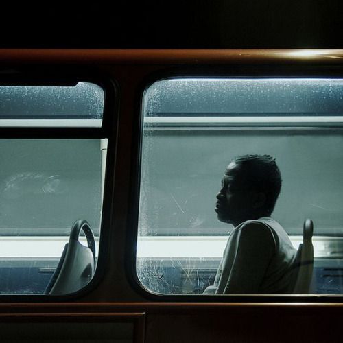 a man sitting on a bus looking out the window at another person standing in front of him