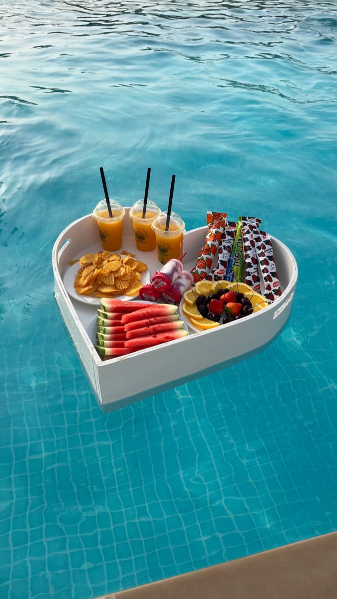 a boat shaped food tray floating on top of a swimming pool with drinks and snacks in it