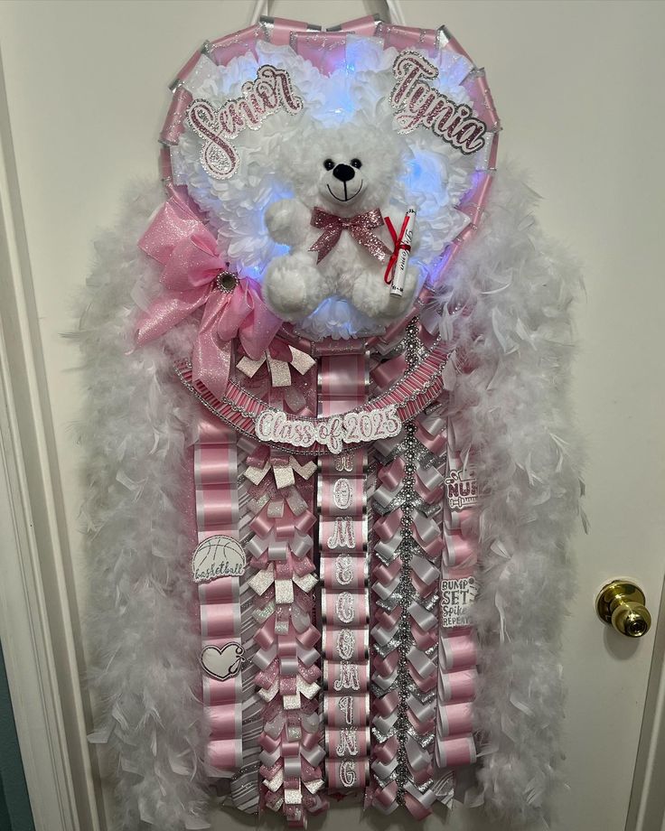 a white teddy bear sitting on top of a pile of pink and silver ribbons next to a door