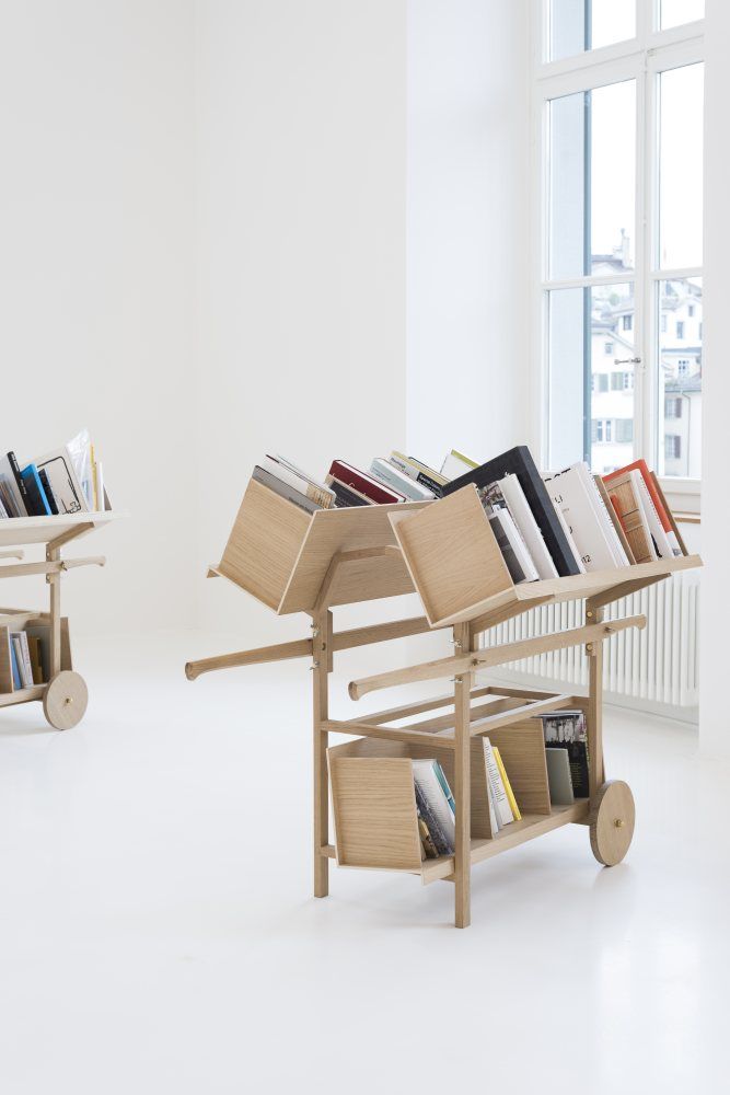 two wooden bookshelves filled with books in front of a white wall next to a window