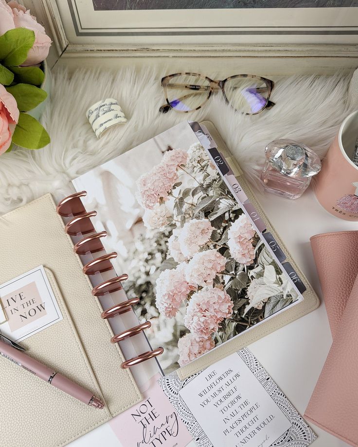 an open planner with pink flowers on it next to a cup of coffee and other items