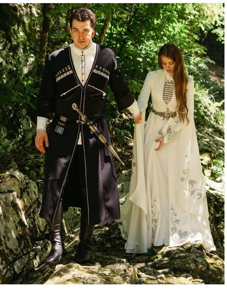 a man and woman dressed up in medieval clothing walking through the woods together, holding hands