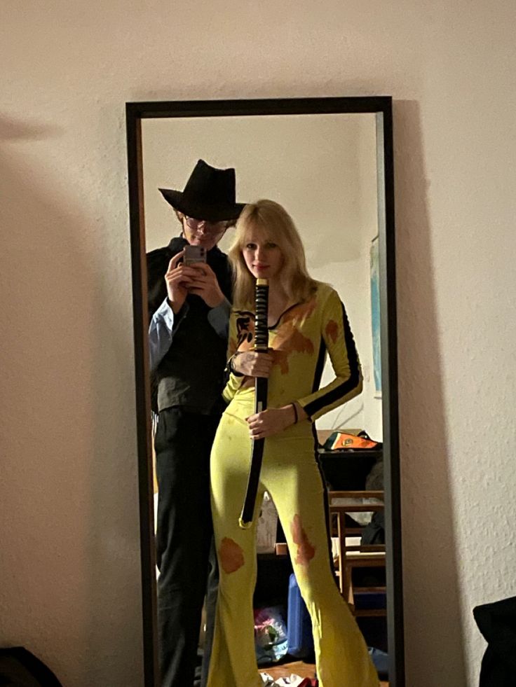 a man standing next to a woman in a yellow dress and cowboy hat looking at her cell phone