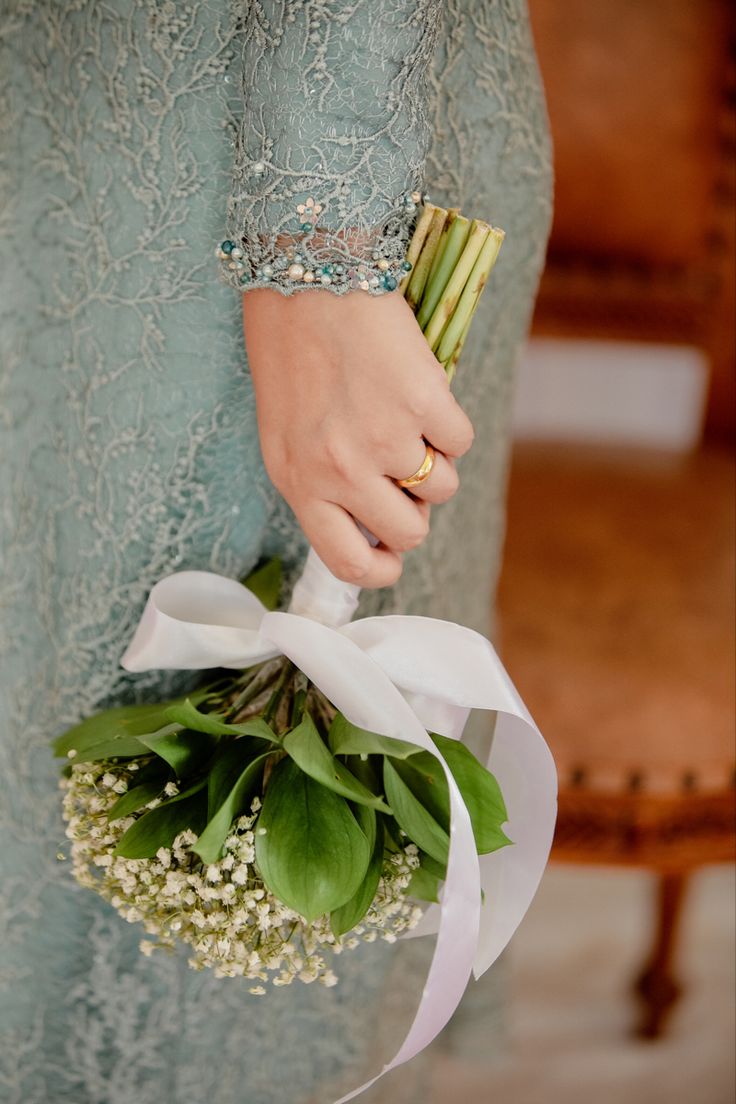 a woman in a blue dress holding a bouquet of flowers and greenery on her arm