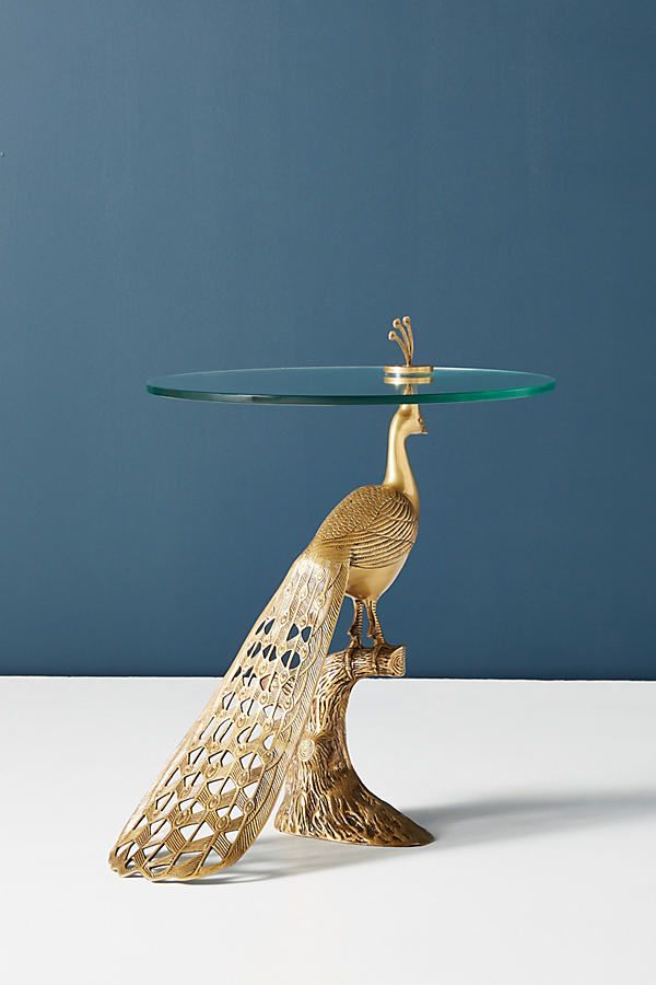 a glass and gold plate with a peacock on it's legs, sitting on a white table