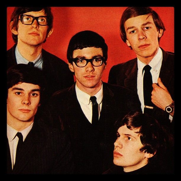 a group of young men standing next to each other in front of a red wall