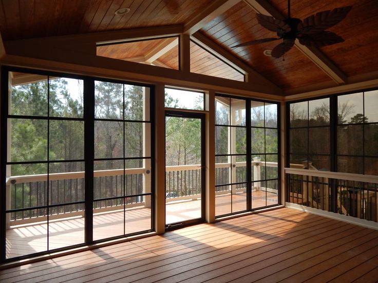 an empty room with wooden floors and large windows on one side, looking out onto the woods