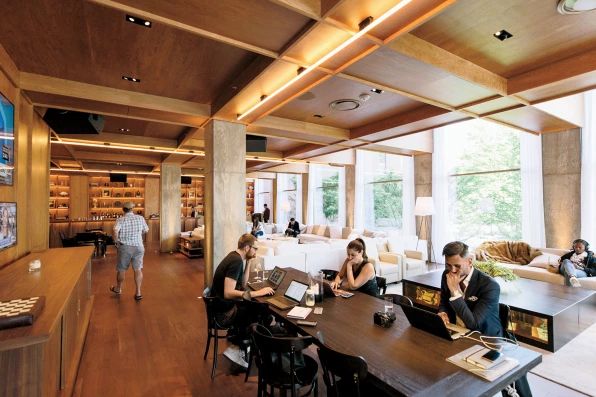 people sitting at tables in a library with bookshelves and couches on the walls