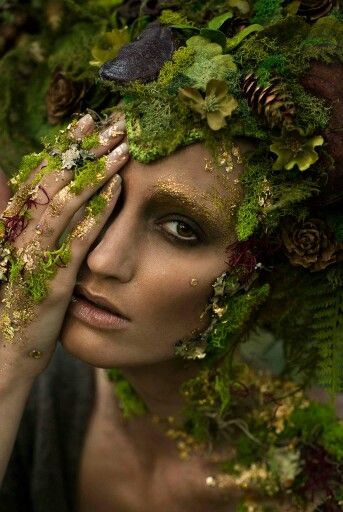 a woman is covered in green plants and leaves with her hands to her face while covering her eyes