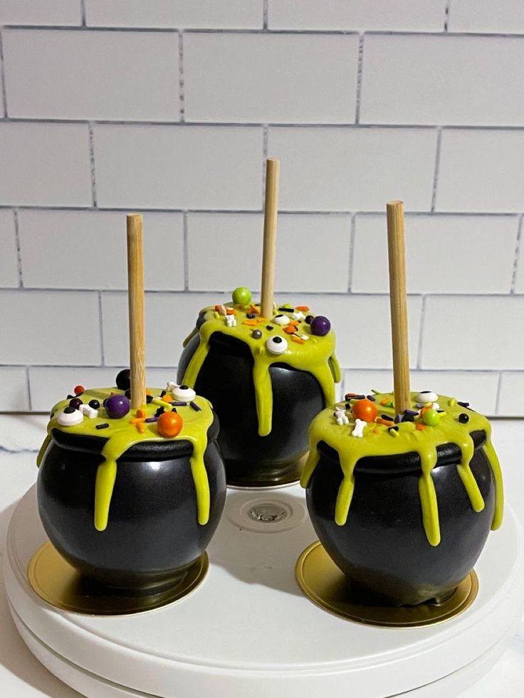 three black pots with yellow icing and sprinkles on them sitting on a white plate