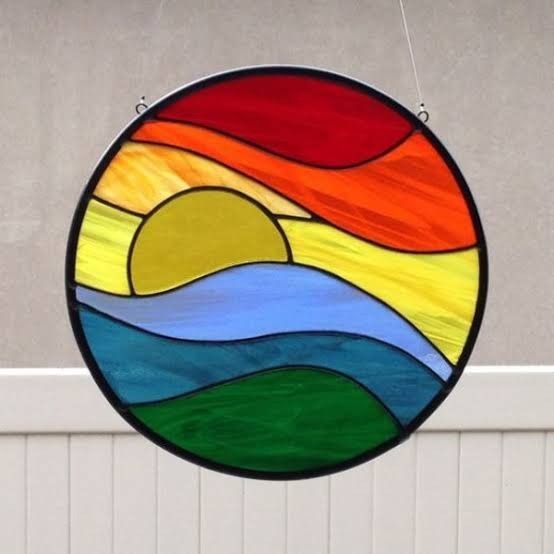 a round stained glass window hanging on the side of a building with mountains and sunset