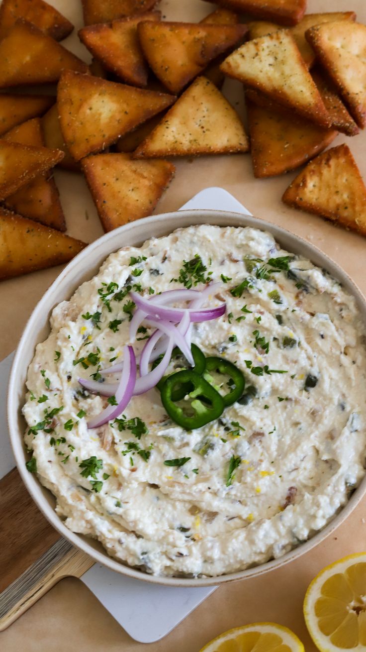 a white bowl filled with dip surrounded by lemon wedges