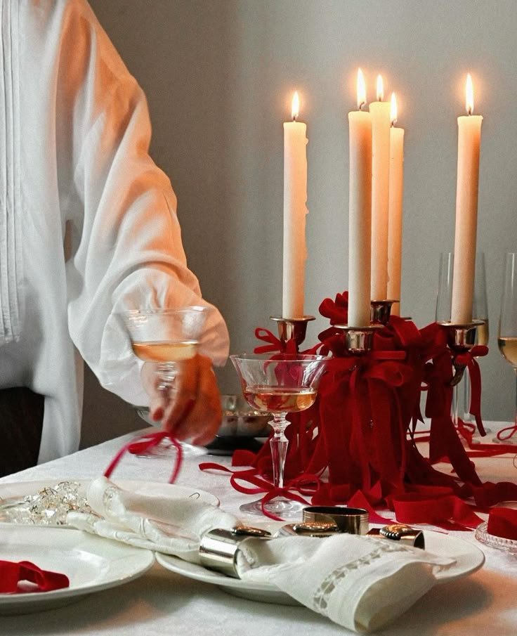 a table topped with candles and plates covered in red ribbon next to glasses filled with wine