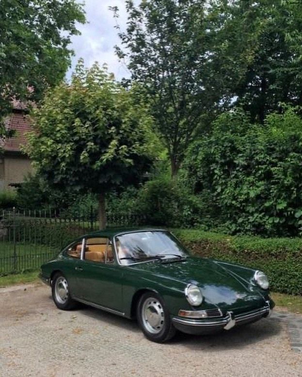 a green porsche sits parked in front of a fenced area with trees and bushes