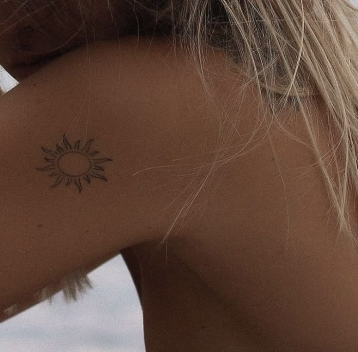 the back of a woman's neck with a small sun tattoo on her left shoulder