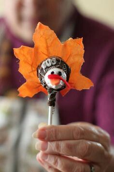 a person holding a candy stick with a snowman on it and an orange leaf