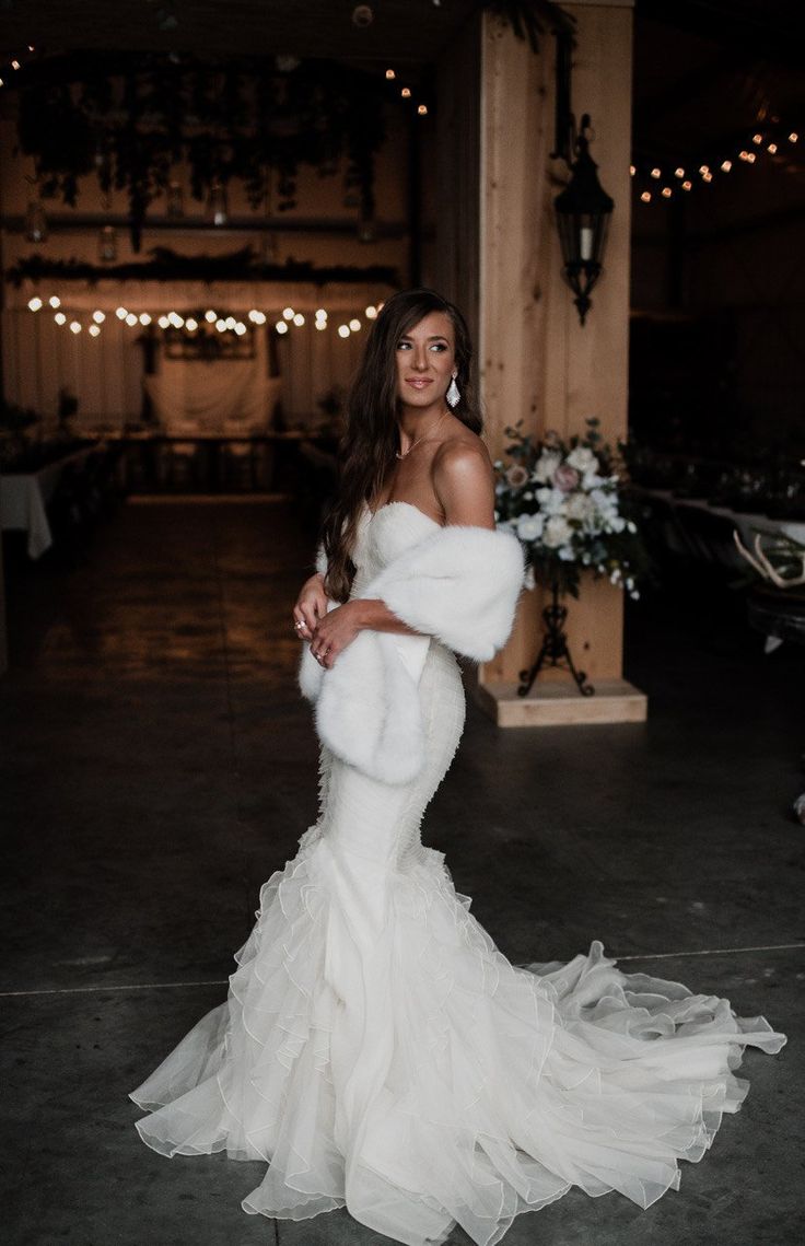 a woman in a white wedding dress posing for the camera with her fur stole around her neck